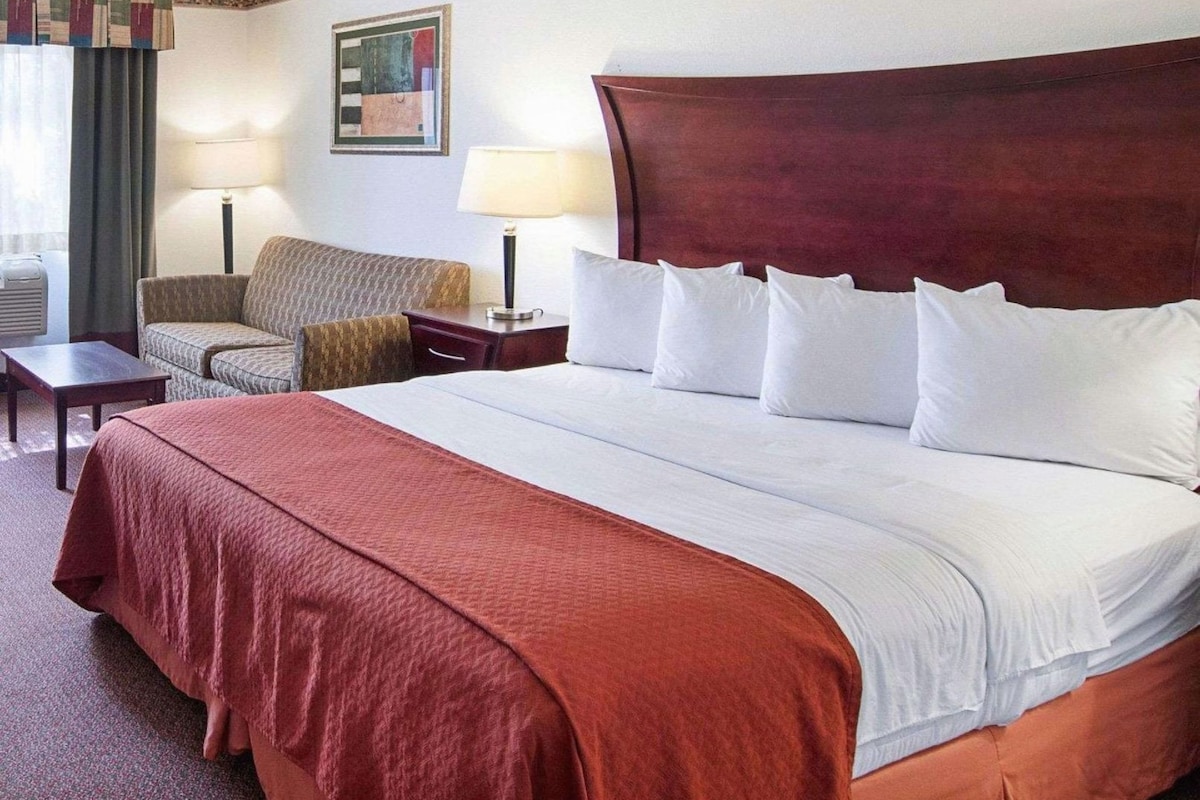 A hotel room with a large bed, a sofa, a desk, and a lamp.