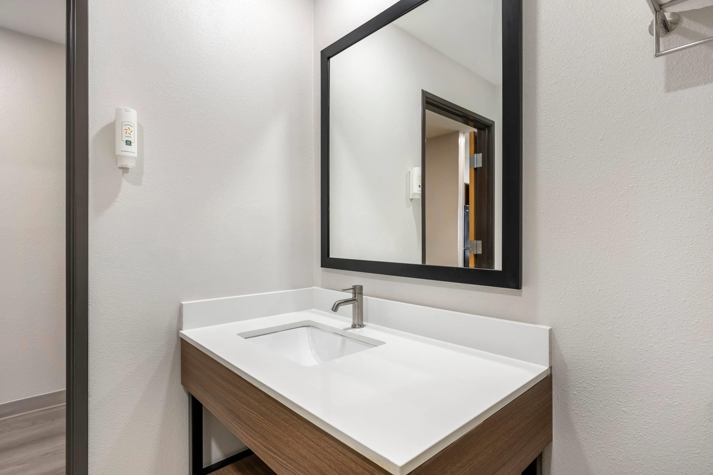 A bathroom with a white sink, a mirror, and a wooden vanity.