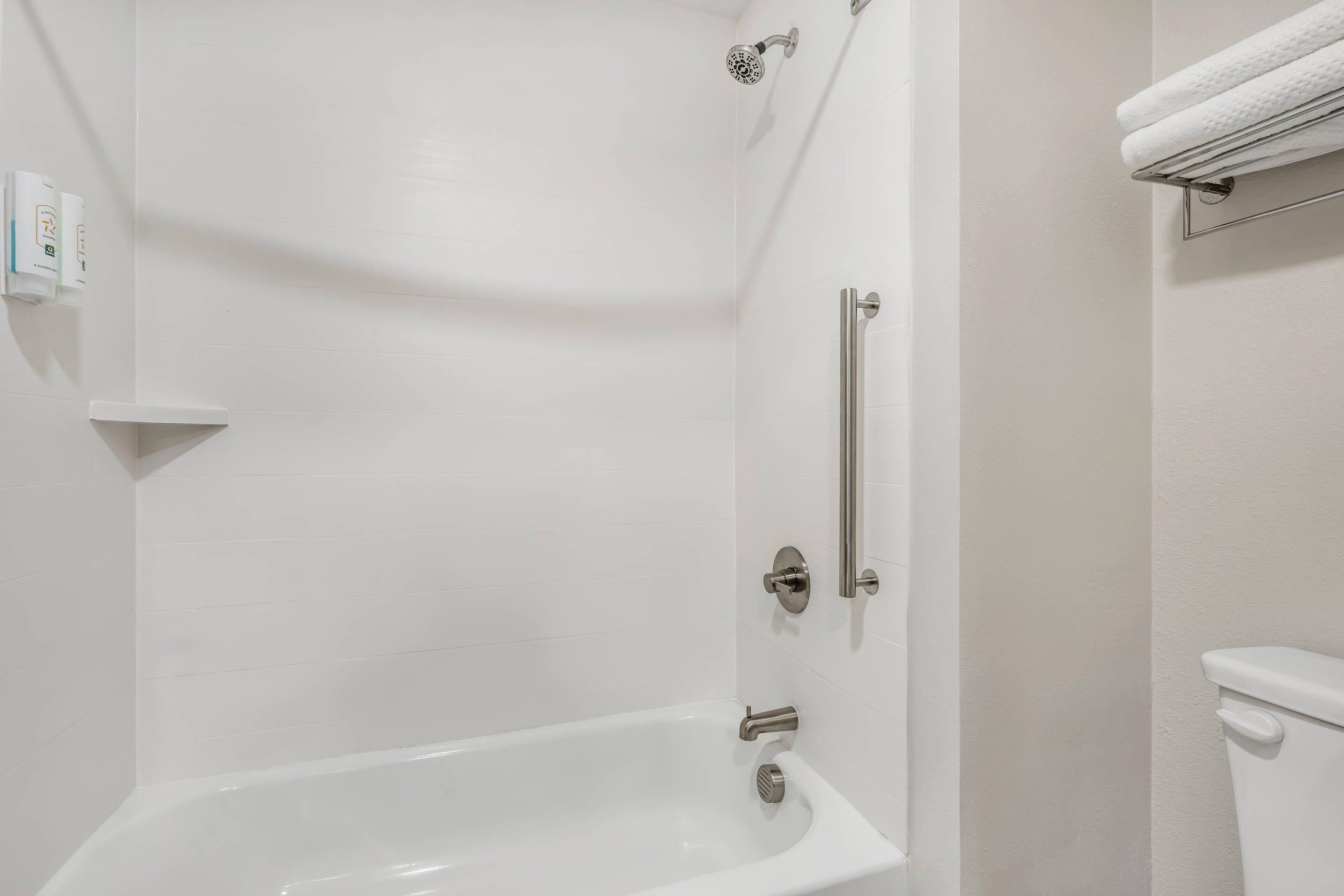 A bathroom with a bathtub, a showerhead, a toilet, and a towel rack.
