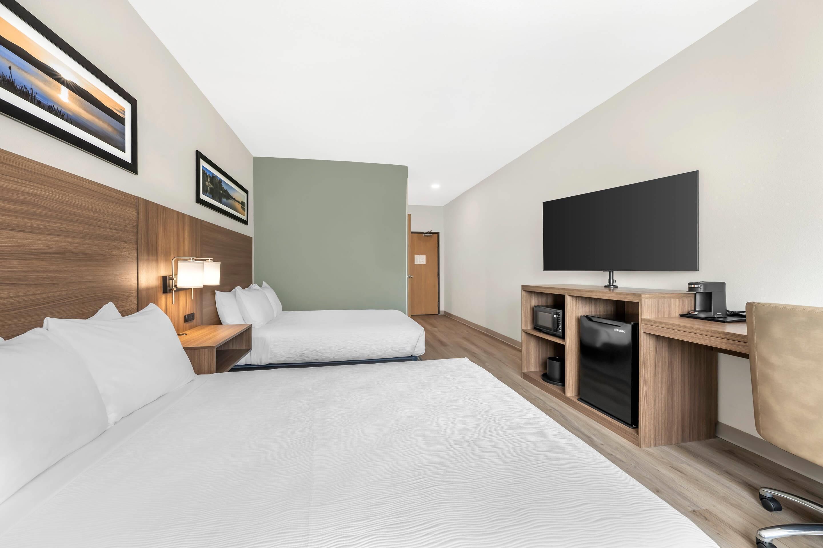 Habitación de hotel con dos camas, televisión, minibar y escritorio con silla.