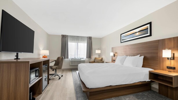 A hotel room with a bed, desk, TV, and a window with curtains.
