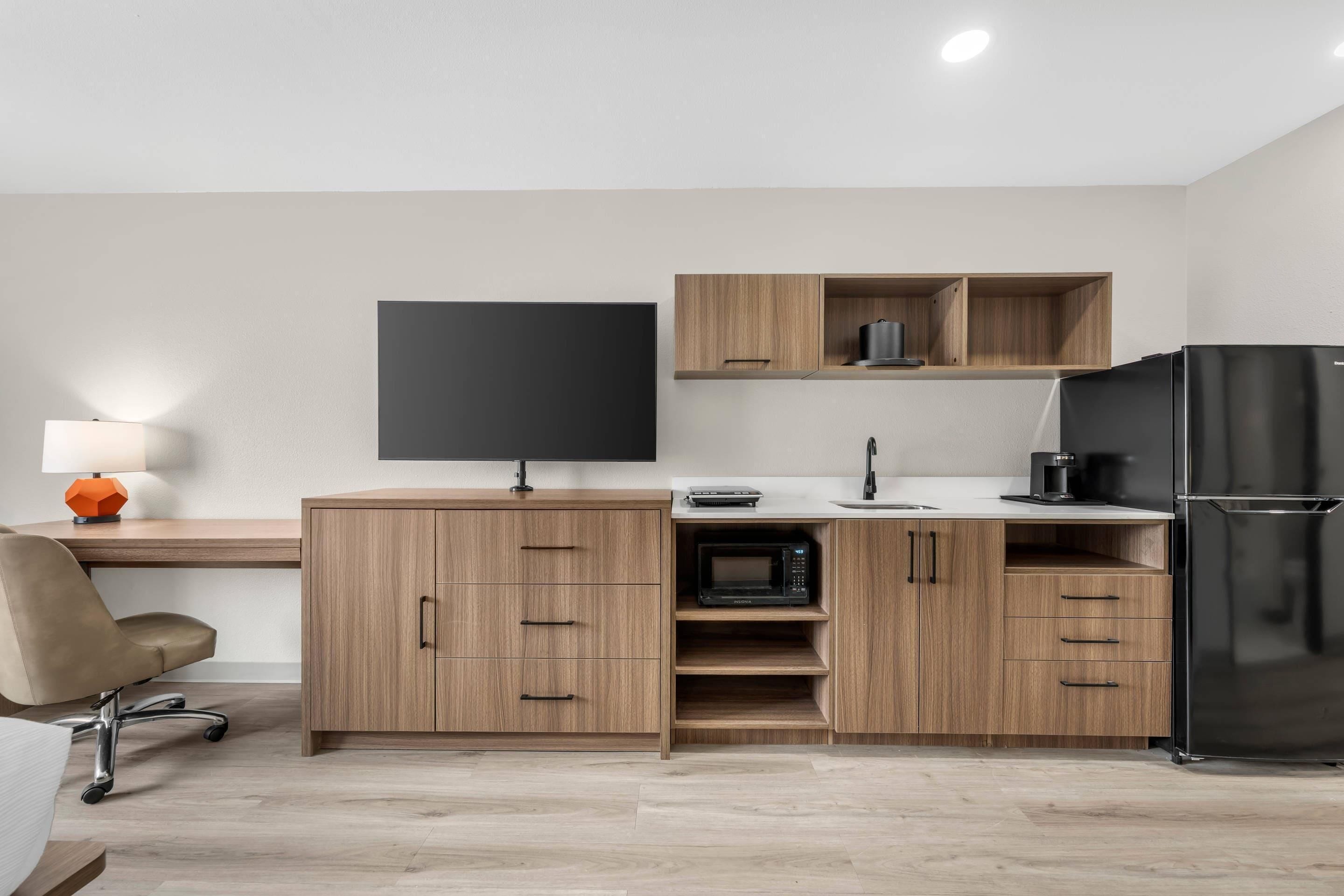 A modern kitchen with wooden cabinets, a black refrigerator, a microwave, and a flat-screen TV.