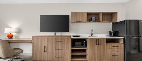 A modern kitchen with wooden cabinets, a black refrigerator, a microwave, and a flat-screen TV.