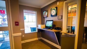 A hotel lobby with a reception desk, a computer, two wall clocks, a fire alarm, and a waste bin.
