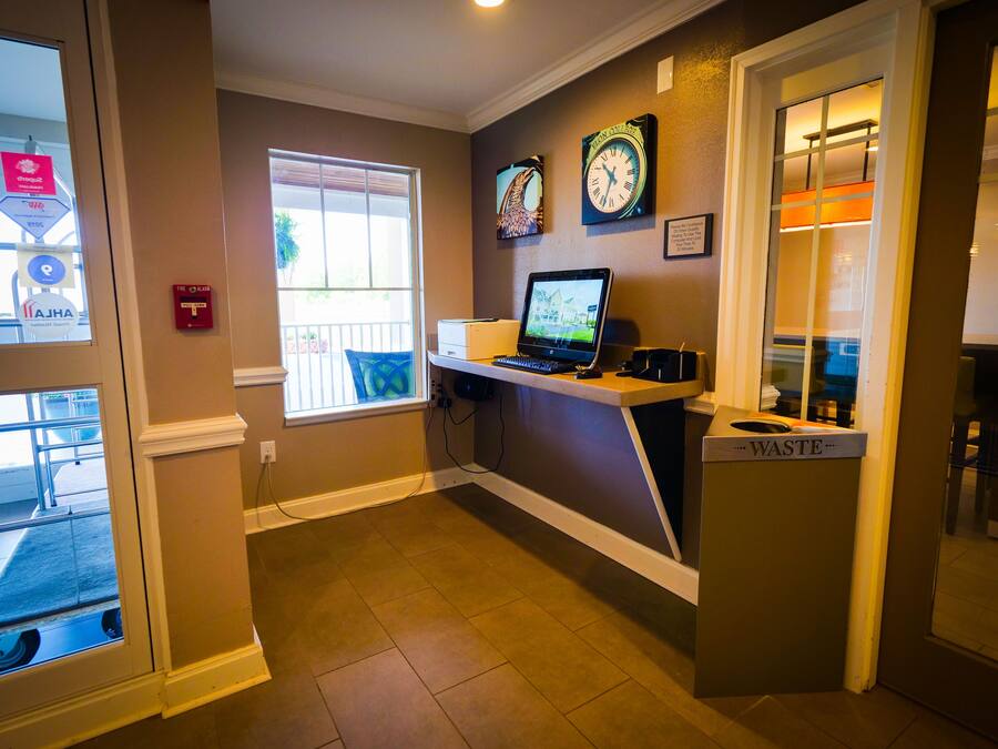 A hotel lobby with a reception desk, a computer, two wall clocks, a fire alarm, and a waste bin.