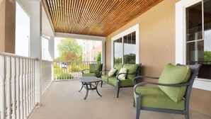 A covered outdoor seating area with two green cushioned chairs and a small table, a wooden ceiling, and a view of the surrounding buildings. - Country Inn & Suites by Radisson, Burlington (Elon), NC (Burlington)