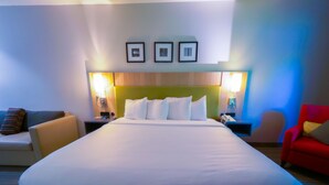 A hotel room with a large bed, two bedside tables, a red armchair, and a sofa. - Country Inn & Suites by Radisson, Burlington (Elon), NC (Burlington)