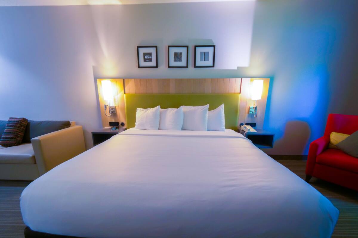 A hotel room with a large bed, two bedside tables, a red armchair, and a sofa.