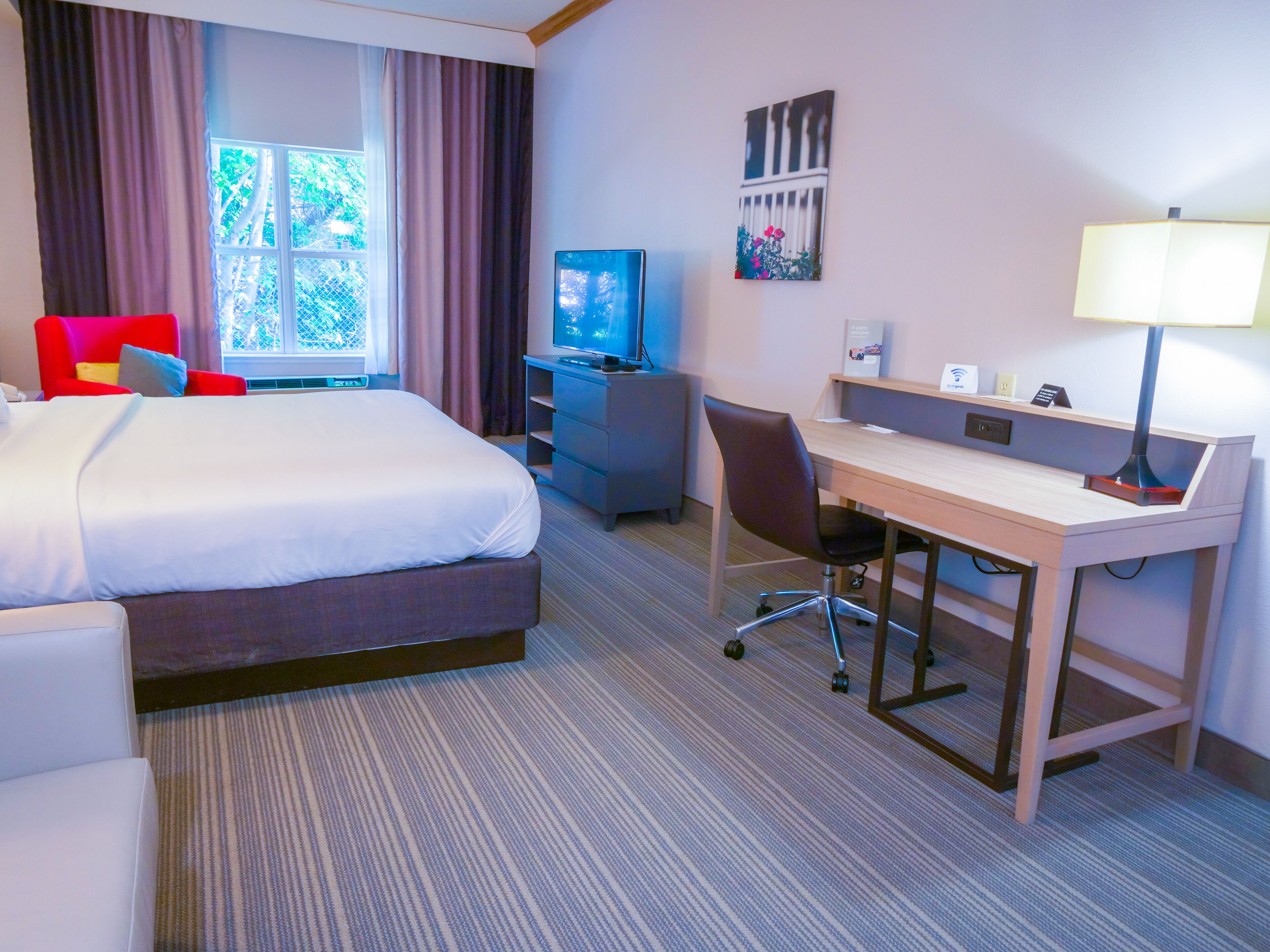A hotel room with a bed, a desk, a chair, a television, and a window with curtains.