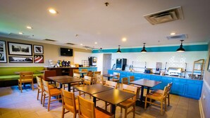 A restaurant with wooden tables and chairs, a counter with a coffee machine, and a blue accent wall. - Country Inn & Suites by Radisson, Burlington (Elon), NC (Burlington)