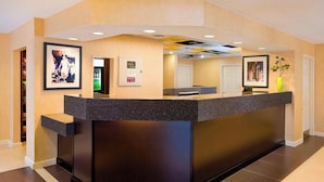 A reception desk with a dark wood finish, a framed photo on the wall, and a small green vase on the counter. - Residence Inn Waco (Waco)