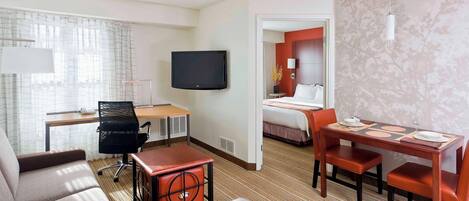 A hotel room with a sofa, a desk with a chair, a TV, a dining table with chairs, and a bed.