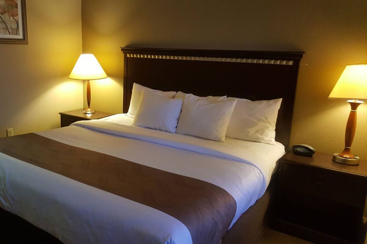 A hotel room with a large bed, two bedside tables, and two lamps.