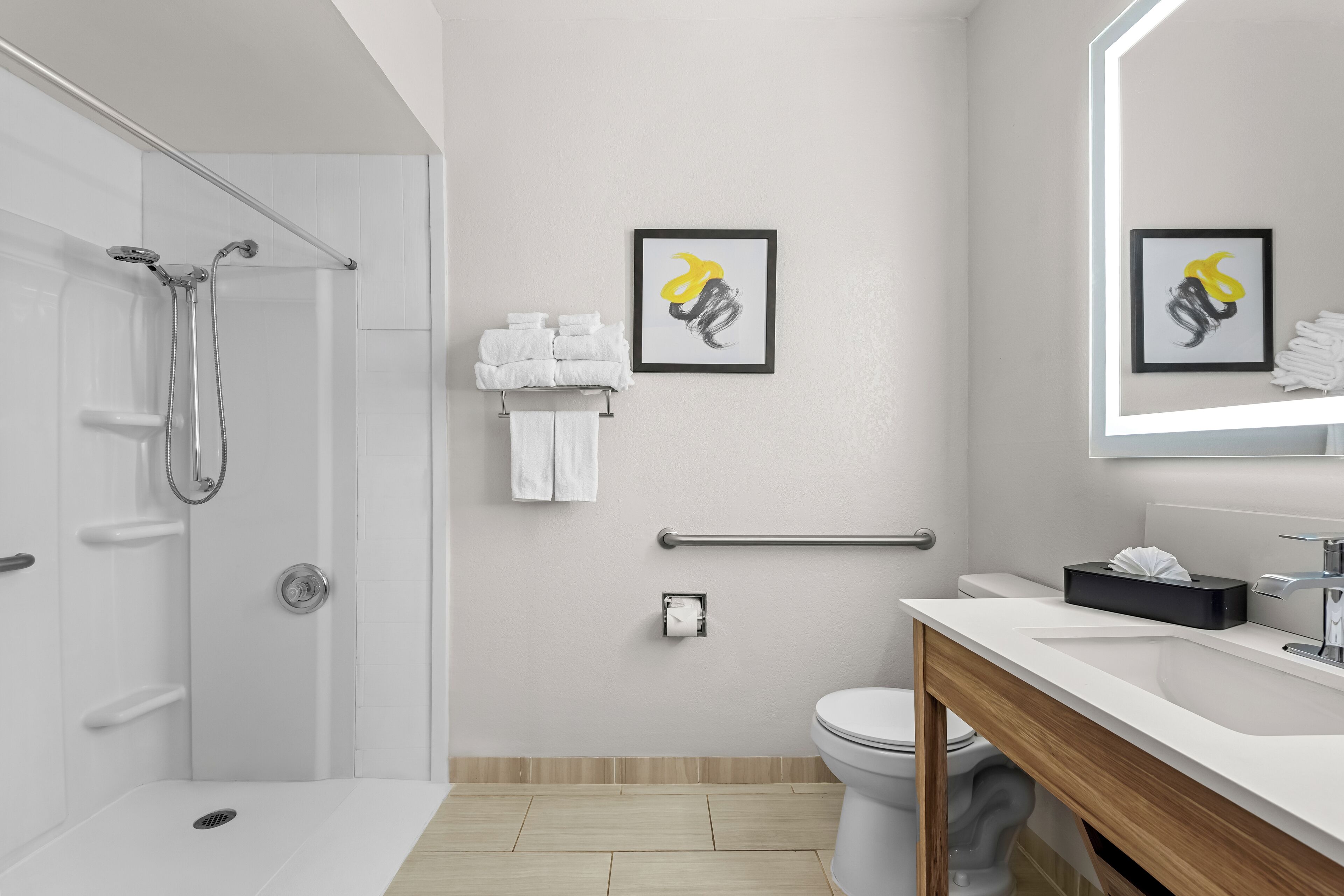 A modern bathroom with a shower, toilet, and sink. There are towels and a framed artwork on the wall.