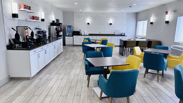 A modern hotel lobby with a kitchen area, seating arrangements, and a coffee station.