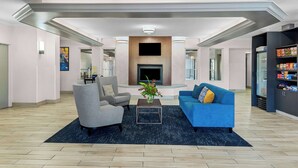 A modern living room with a fireplace, a blue sofa, a grey armchair, and a coffee table with a vase of flowers.