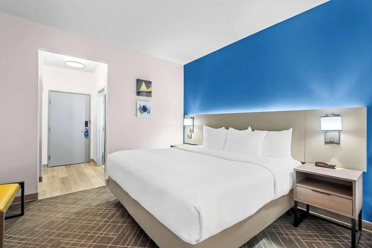 A hotel room with a large bed, a nightstand, a bedside table, a door, and a wall with a blue accent.