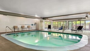 An indoor swimming pool with a clear water surface, surrounded by lounge chairs and a tiled floor.