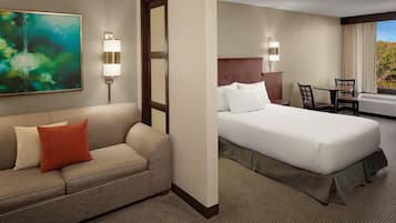 A hotel room with a bed, a sofa, a desk, and a painting on the wall.