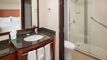 A hotel bathroom with a marble sink, a mirror, a toilet, and a glass-enclosed shower.