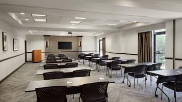 A conference room with tables and chairs, a podium, a projector screen, and large windows.