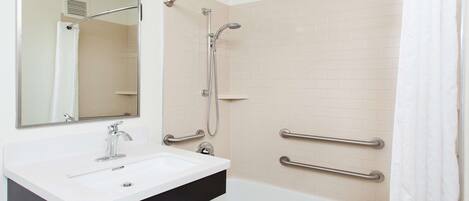 A bathroom with a white sink, a mirror, a shower with a handheld showerhead, and grab bars on the walls.