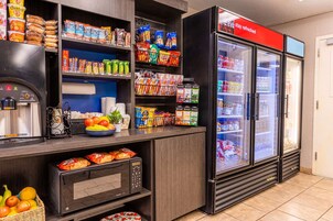 Un área de comida autoservicio con una máquina de café, microondas y refrigerador llenos de aperitivos y bebidas.