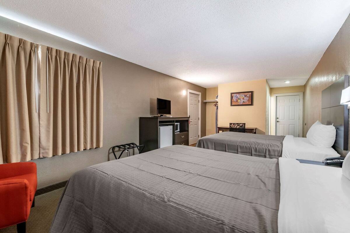A hotel room with two beds, a desk, a television, and a chair.