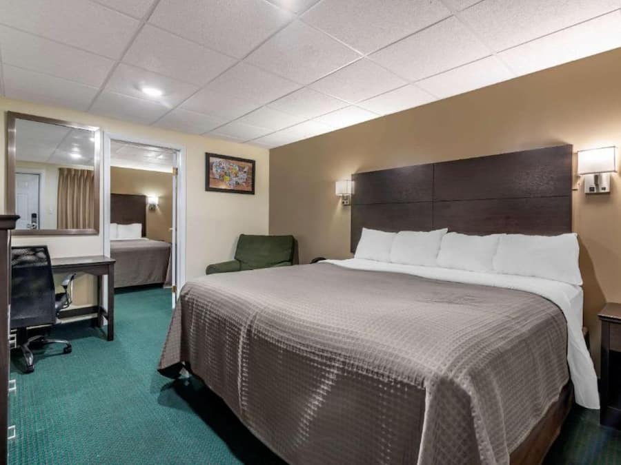 A hotel room with a large bed, a desk, a chair, a mirror, and a painting on the wall.