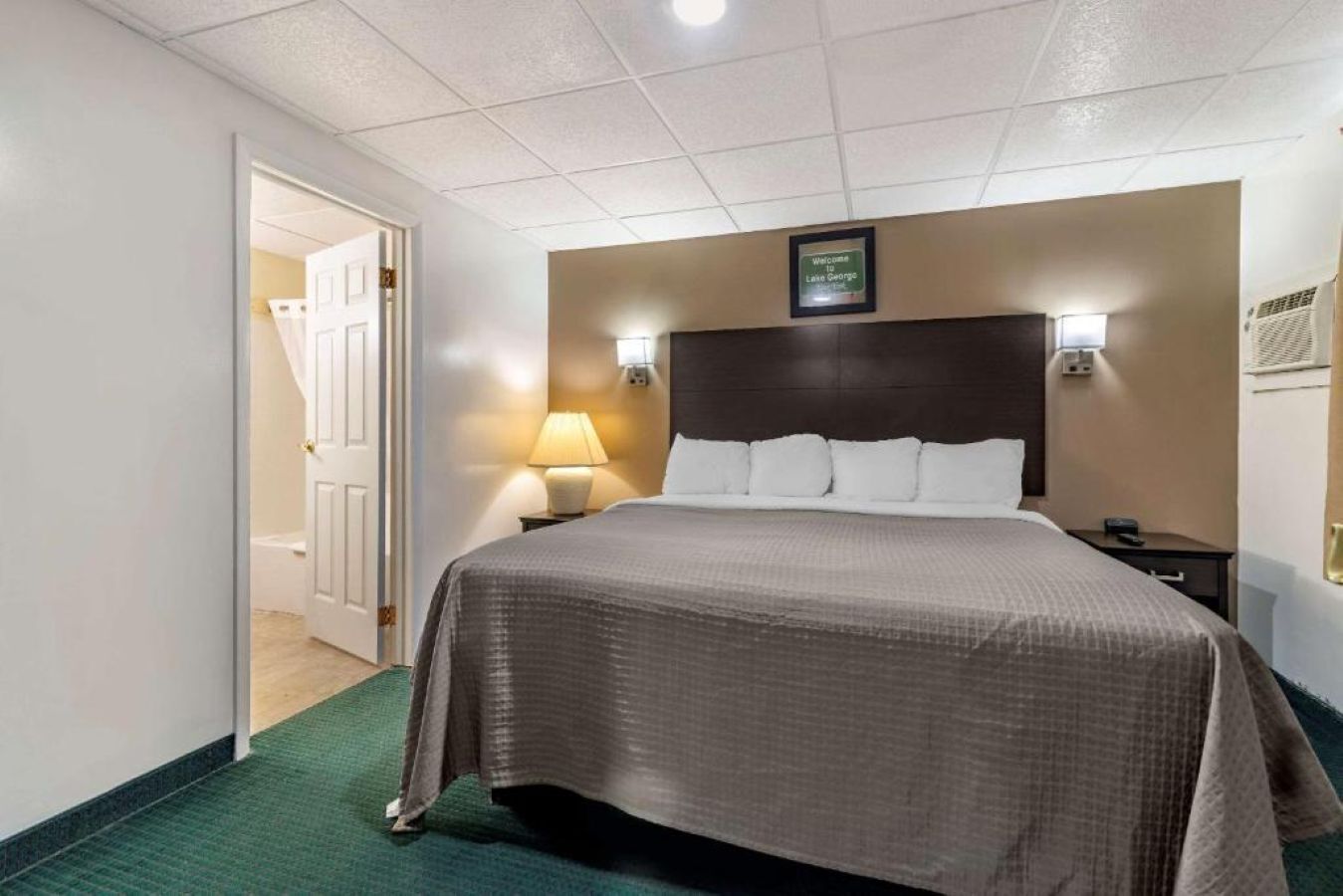 Een hotelkamer met een bed, nachtlampjes, een hoofdbord en een deur naar een badkamer.