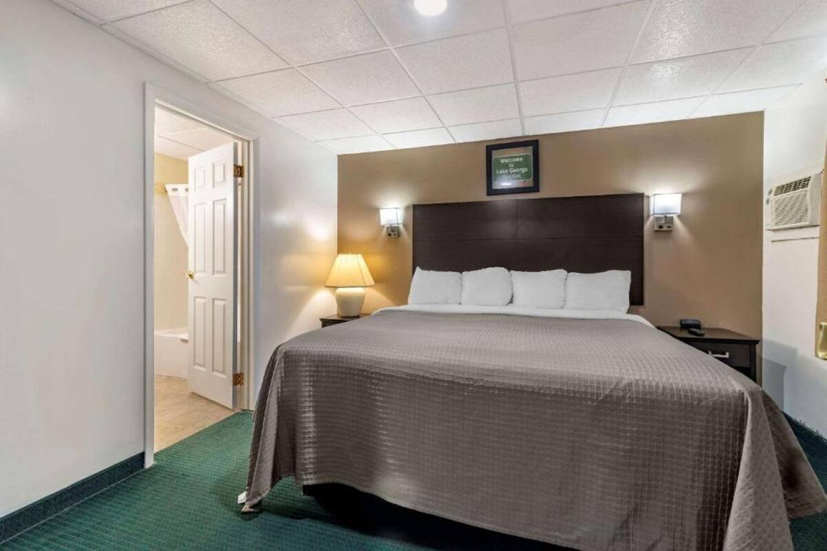 A hotel room with a bed, bedside lamps, a headboard, and a door leading to a bathroom.
