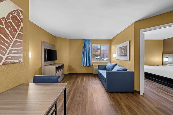 A modern hotel room with a wooden floor, a sofa, a TV, and a bed. - Suburban Studios Charlotte – Executive Park (Charlotte)
