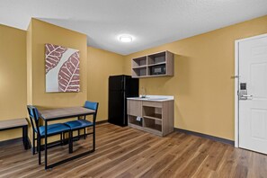 A compact kitchen with a microwave, refrigerator, and a small sink. There is a dining table with chairs and a bench. - Suburban Studios Charlotte – Executive Park (Charlotte)