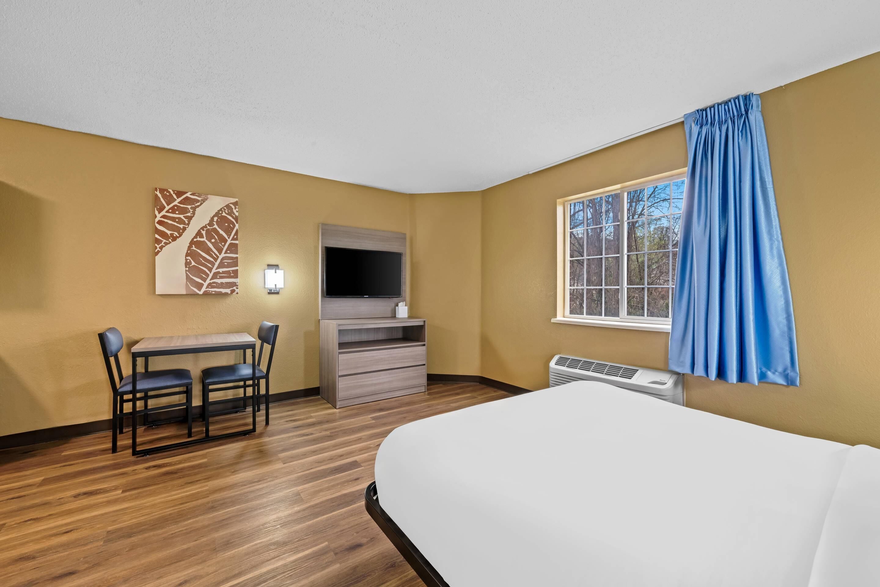 Ein Hotelzimmer mit einem Bett, einem Schreibtisch mit Stuhl, einem Flachbildfernseher und einem Fenster mit Vorhängen.