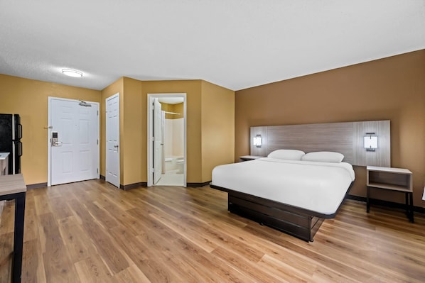 Habitación de hotel con una cama grande, una mesita de noche, un armario y un baño con ducha e inodoro.