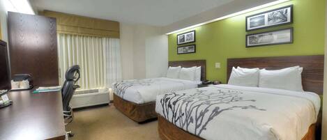 Habitación de hotel con dos camas, un escritorio con silla, un calentador y cuadros en la pared.