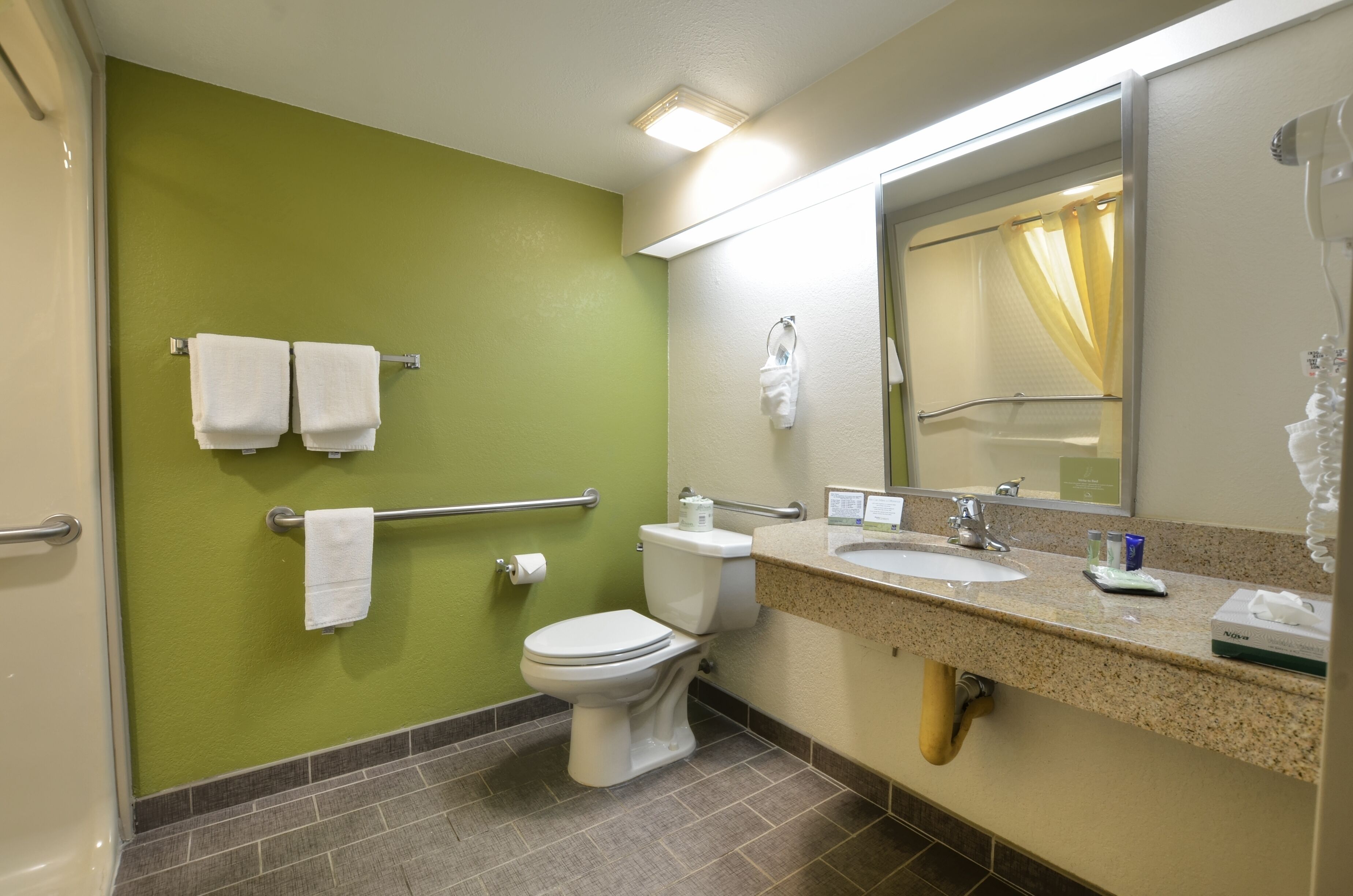 A bathroom with a green wall, white toilet, and sink with a mirror above.