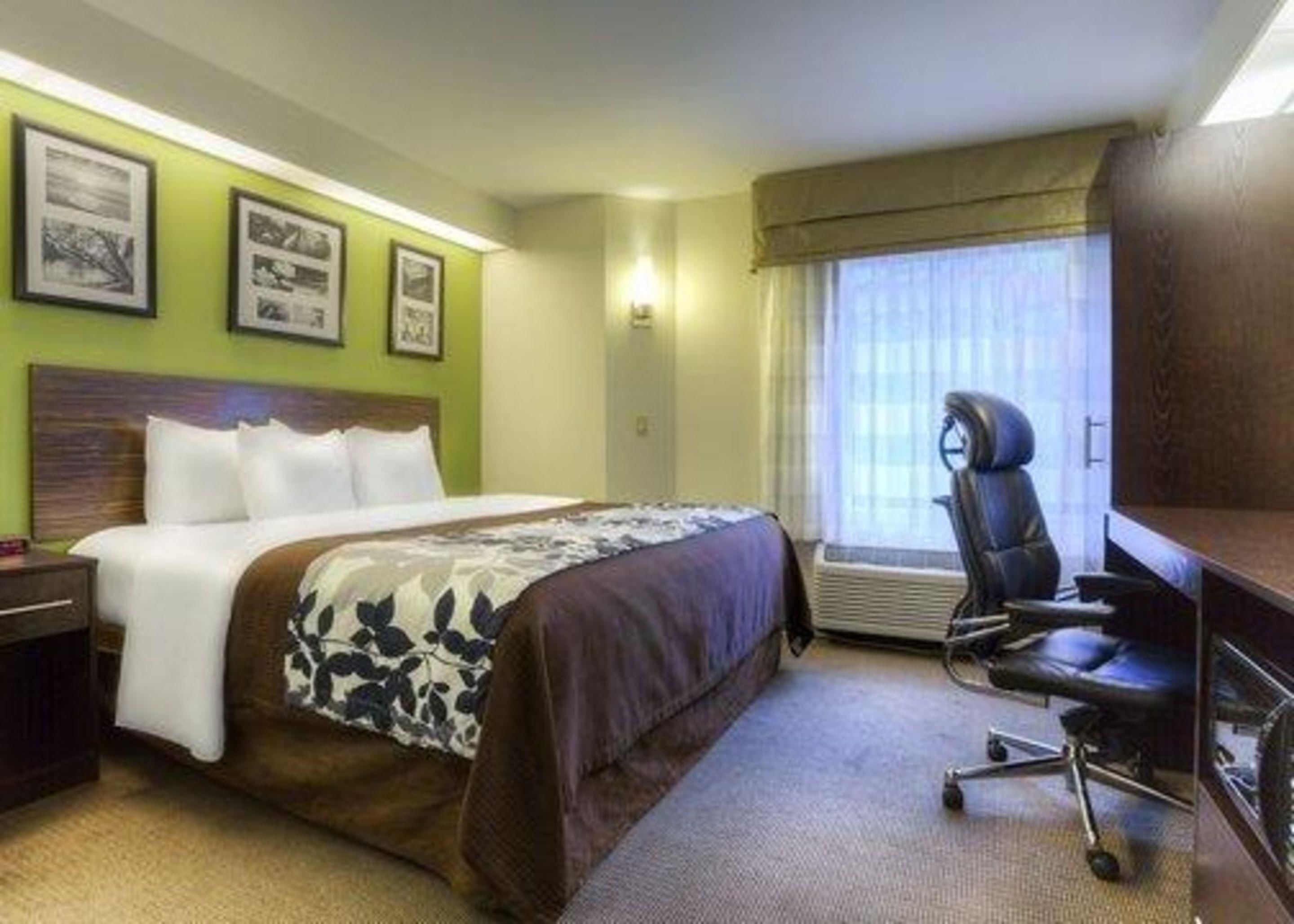 Quarto de hotel com cama, escrivaninha, cadeira e janela com cortinas.