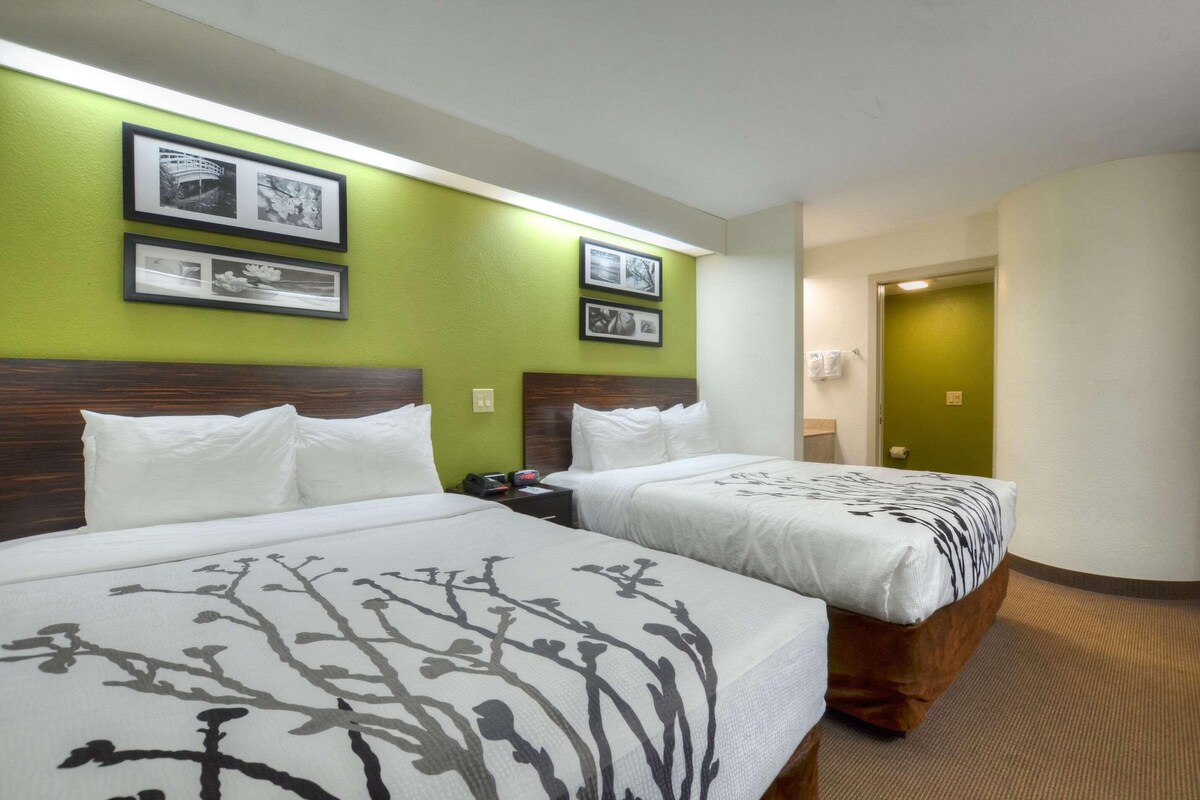 A hotel room with two beds, green walls, framed pictures, and a wooden headboard.