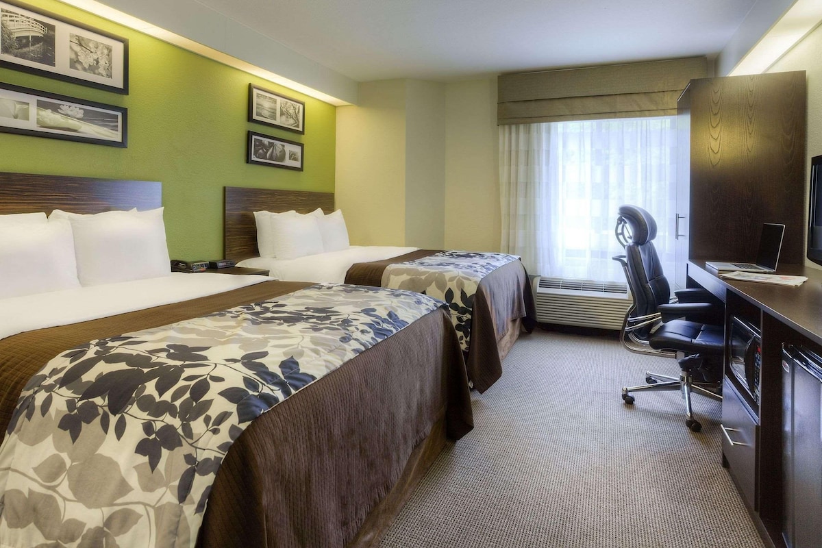 A hotel room with two beds, a desk with a laptop, a chair, and a television.