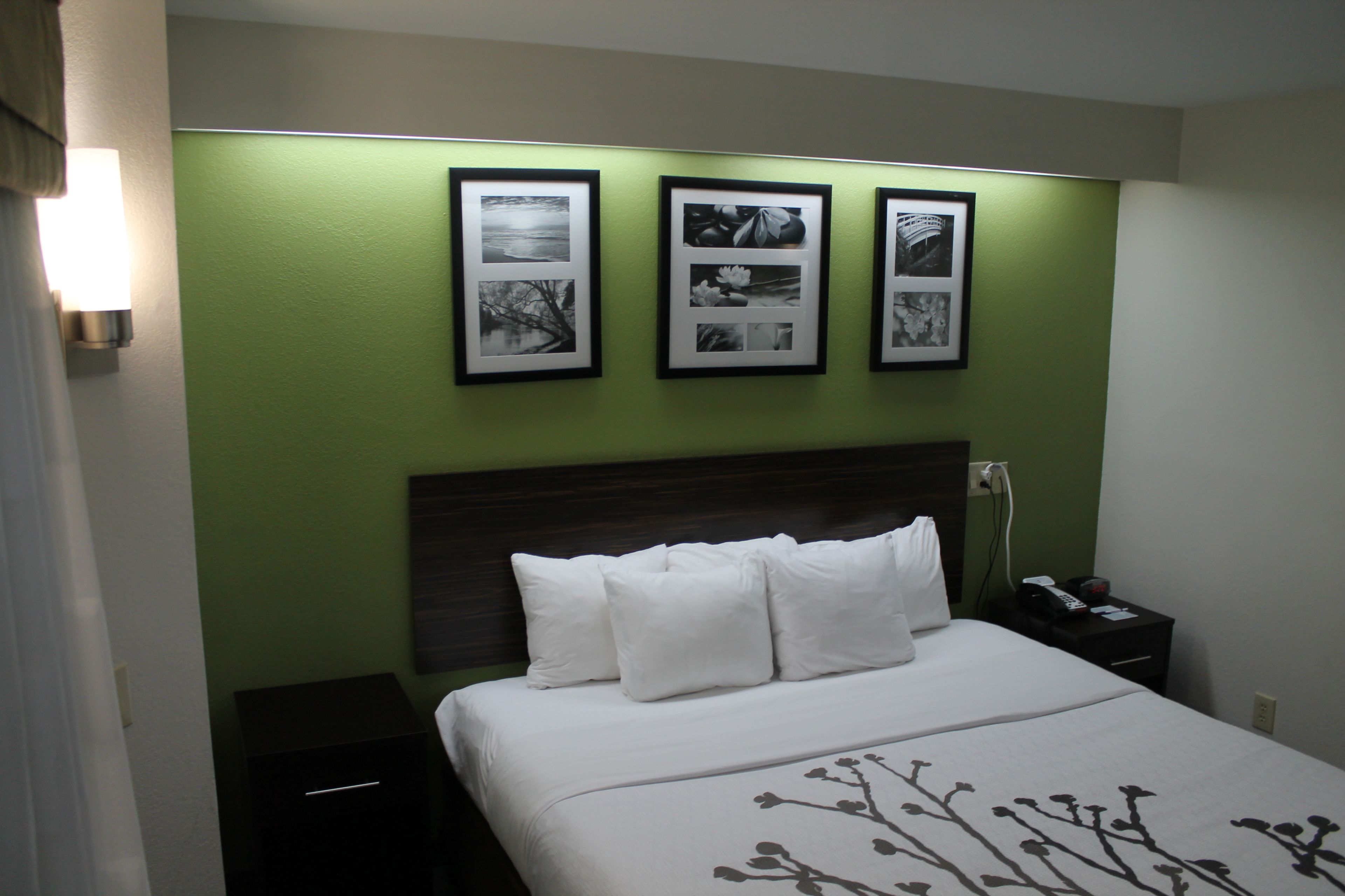 Una habitación de hotel con una cama, una mesita de noche y una lámpara de pared.