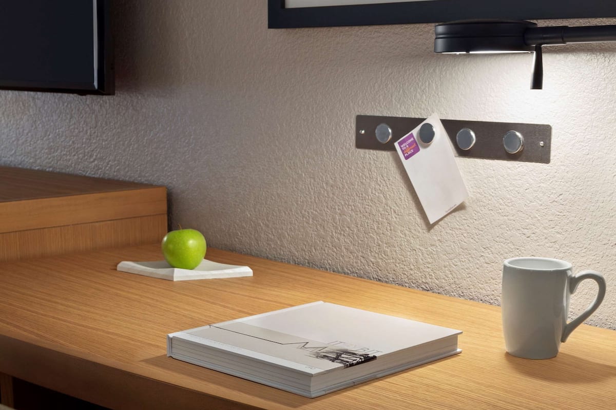 A neatly arranged desk with a book, a mug, and a green apple on a coaster.