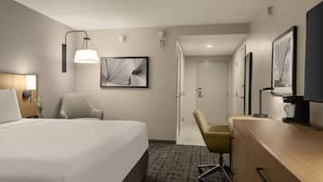 Habitación de hotel con una cama grande, dos sillones, un escritorio y obras de arte en las paredes.