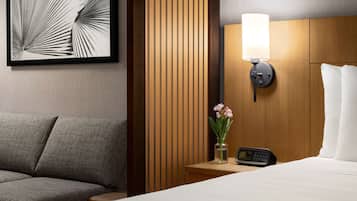 A hotel room with a bed, a nightstand with a lamp, a vase with flowers, and a framed picture on the wall.