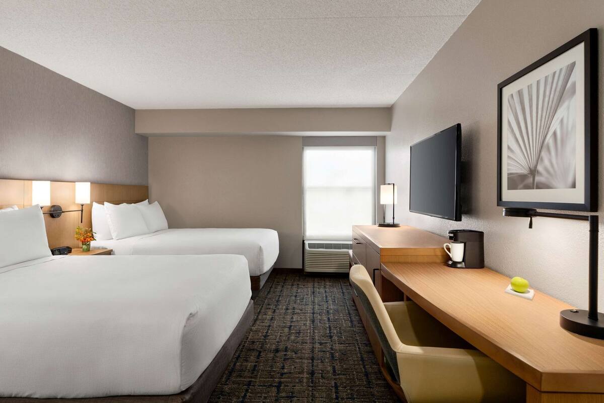 A hotel room with two beds, a desk with a chair, a television, and a window with a view.