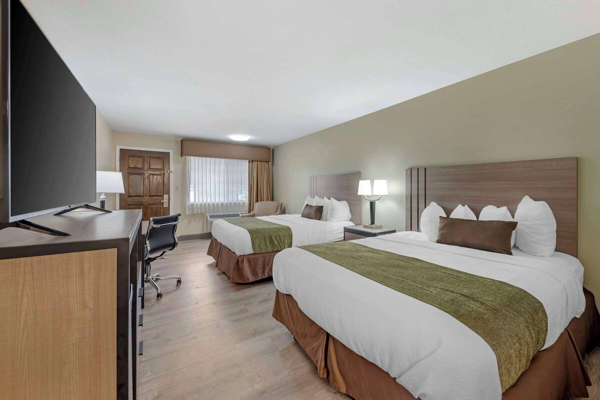 A hotel room with two beds, a desk, a chair, and a TV.