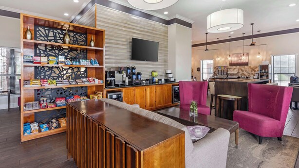 Een moderne hotellobby met een houten receptiebalie, een grote televisie aan de muur en een bar met zitplaatsen.