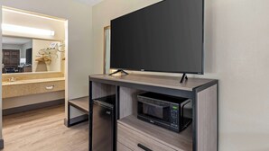 Een moderne badkamer met een grote spiegel, een flatscreen televisie bevestigd aan een houten kast, een magnetron en een kleine koelkast.
