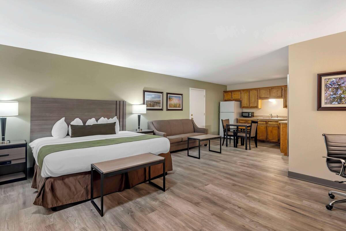 A hotel room with a bed, bedside tables, a sofa, a desk, and a kitchenette.