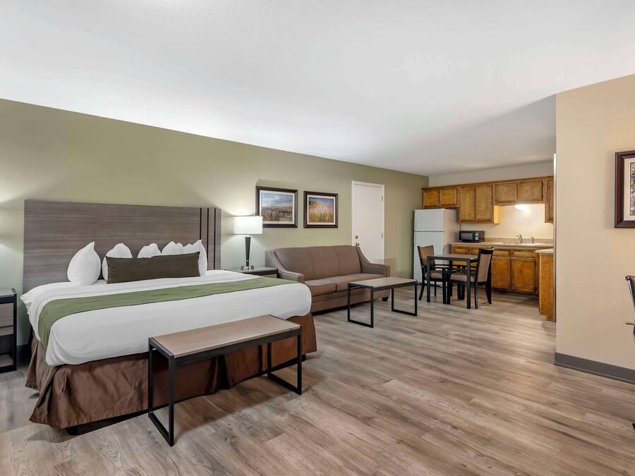 Una habitación de hotel con cama, mesitas de noche, sofá, escritorio y kitchenette.